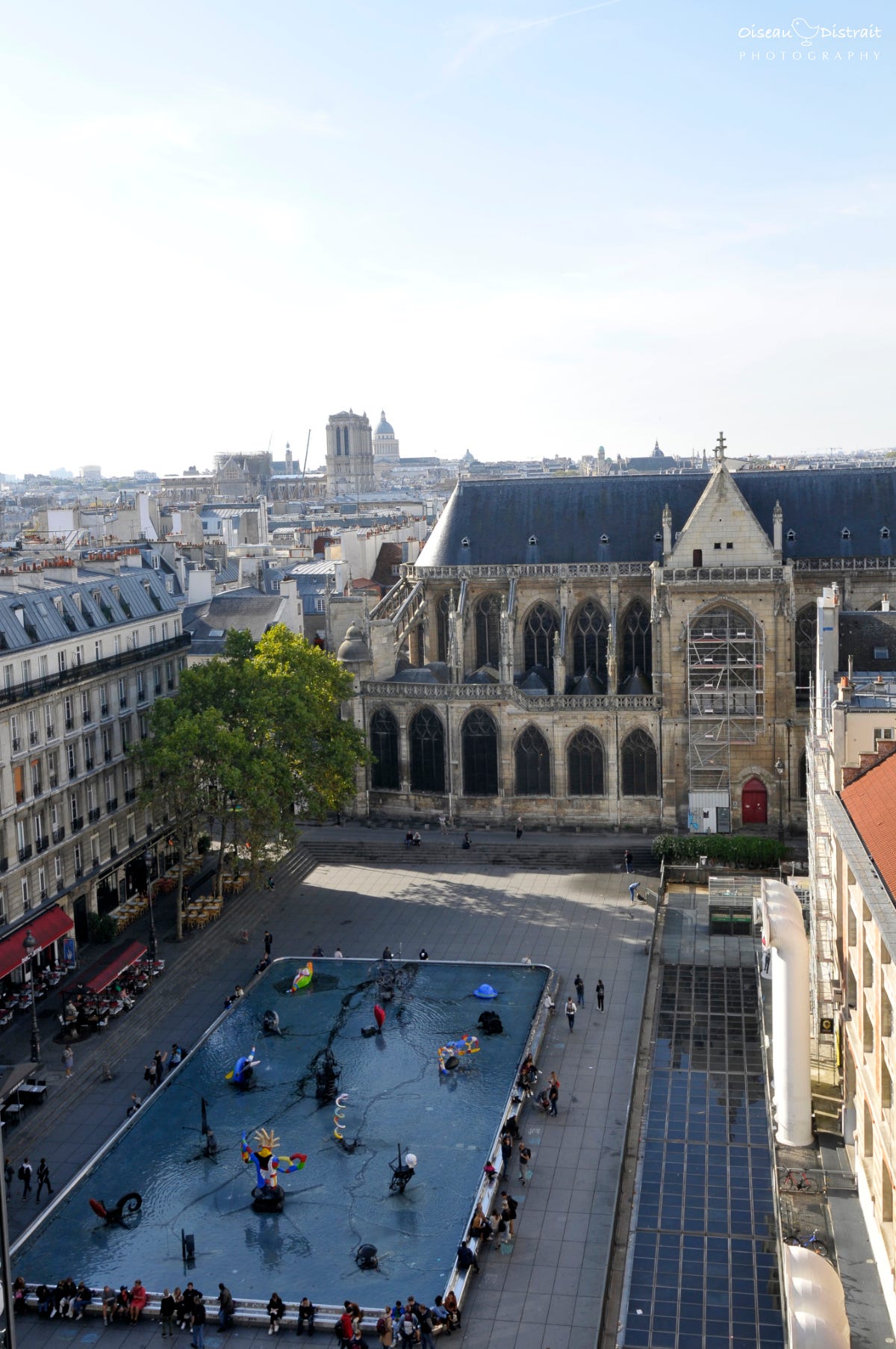 A bird's eye view from high to an outdoor square with fountain full of sculpture under a sunny sky. A plaza between the historical building and a modern museum, in Paris. A bird's eye view from high to an outdoor square with fountain full of sculpture under a sunny sky. A plaza between the historical building and a modern museum, in Paris.