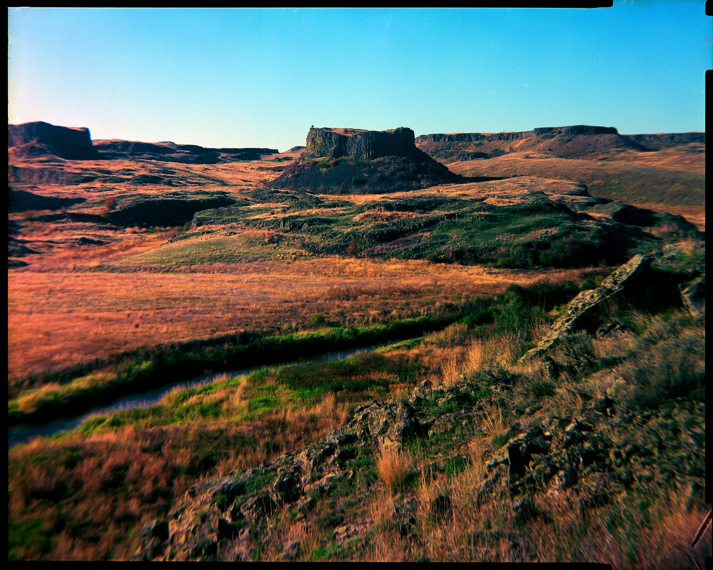 A small stream cuts through a field before a few basalt rock formations.