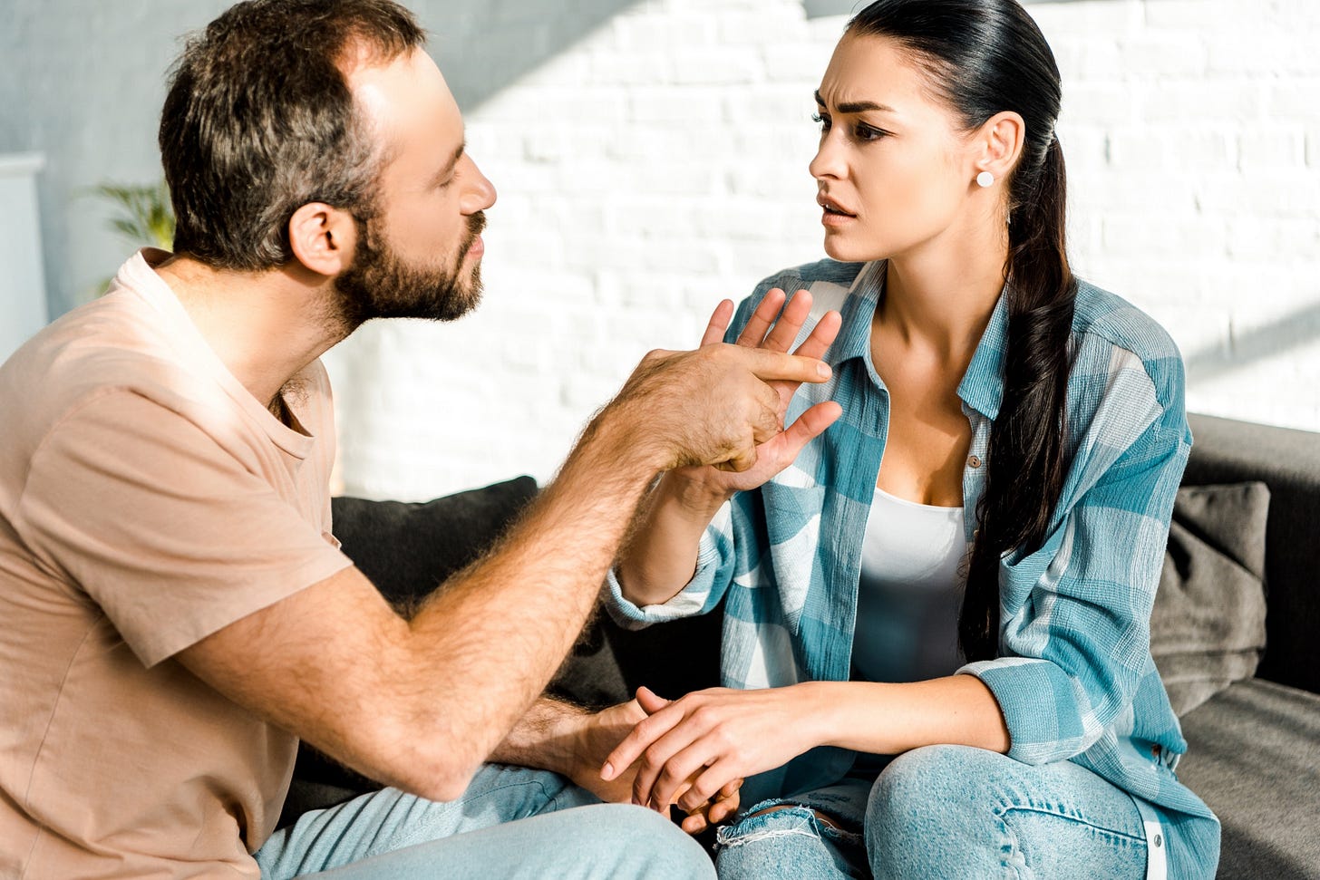 A couple sits on a couch in the middle of a heated argument.