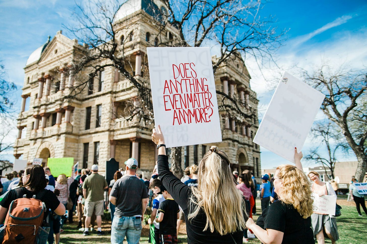 a woman at a protest with a sign that says "Does anything matter anymore?"
