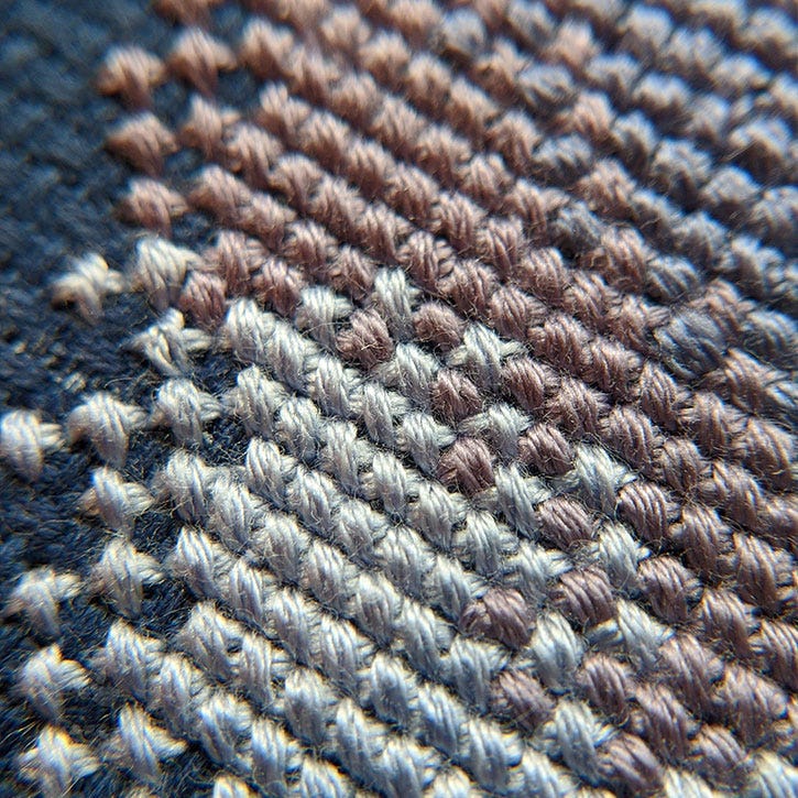 A very close-up photograph of cross-stitch stitches in a few different colours. Stitched on navy Aida fabric. A very close-up photograph of cross-stitch stitches in a few different colours. Stitched on navy Aida fabric.