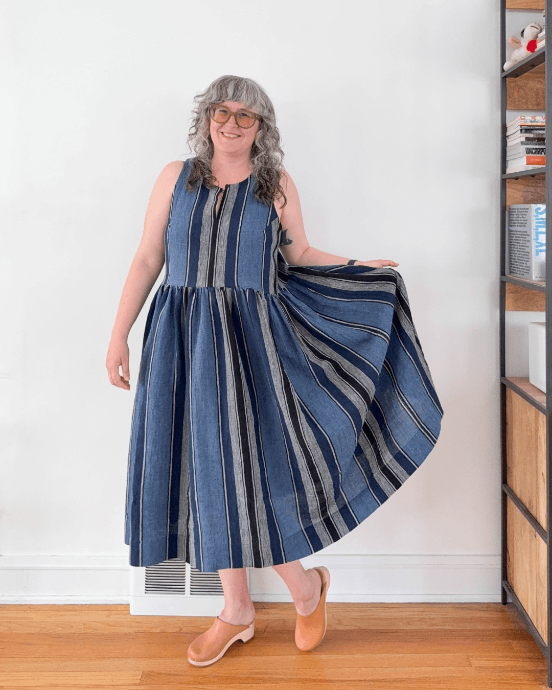 Woman smiling and holding out full skirt of blue striped linen Austin Dress View B without button bands showing gathered skirt volume