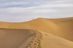 A high desert sand dune with a tiny human figure at its crest.