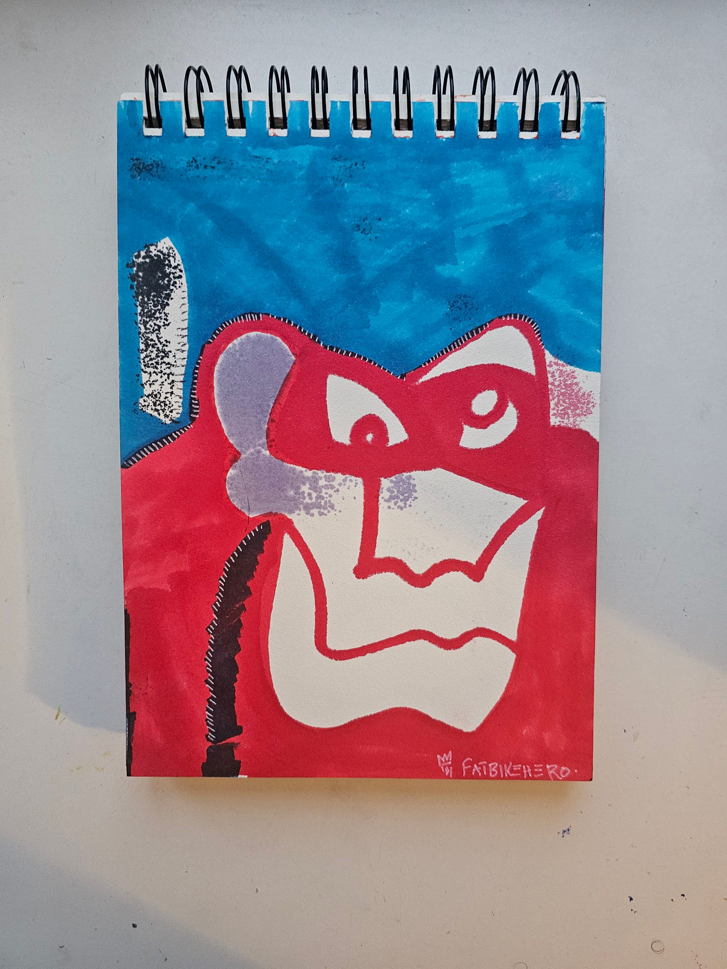 A neo-expressionist sketchbook drawing by Fatbikehero titled "The Scheemer." The artwork features a stylized, abstract face of an ape or gorilla rendered in bold red marker against a textured blue background, with white negative space forming the facial features. A neo-expressionist sketchbook drawing by Fatbikehero titled "The Scheemer." The artwork features a stylized, abstract face of an ape or gorilla rendered in bold red marker against a textured blue background, with white negative space forming the facial features.