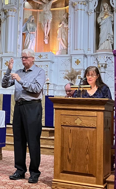 Three photos are shown, are all of white individuals in a church sanctuary with a white altar and a large cross behind them. The first image at left shows a white woman in a navy blue dress with curly auburn hair. She is using sign language. She’s wearing glasses. In the next image a man with white hair and a light grey button-down dress shirt. He’s also speaking in sign language next to a woman at a podium making an announcement. She has long brown hair. Both are wearing glasses. At the right are two women singing in sign language, one on the left has short blond hair and is wearing a purple sweatshirt, the other is wearing a dark colored dress and has curly brown hair. 
