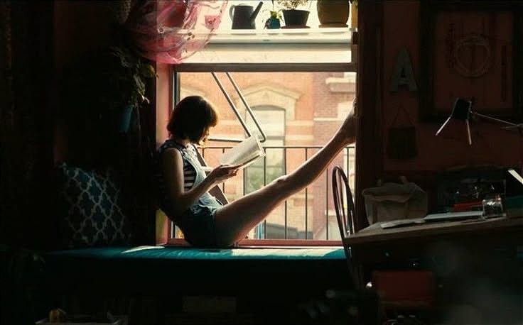 This may contain: a woman sitting on top of a bed next to a window with her legs crossed