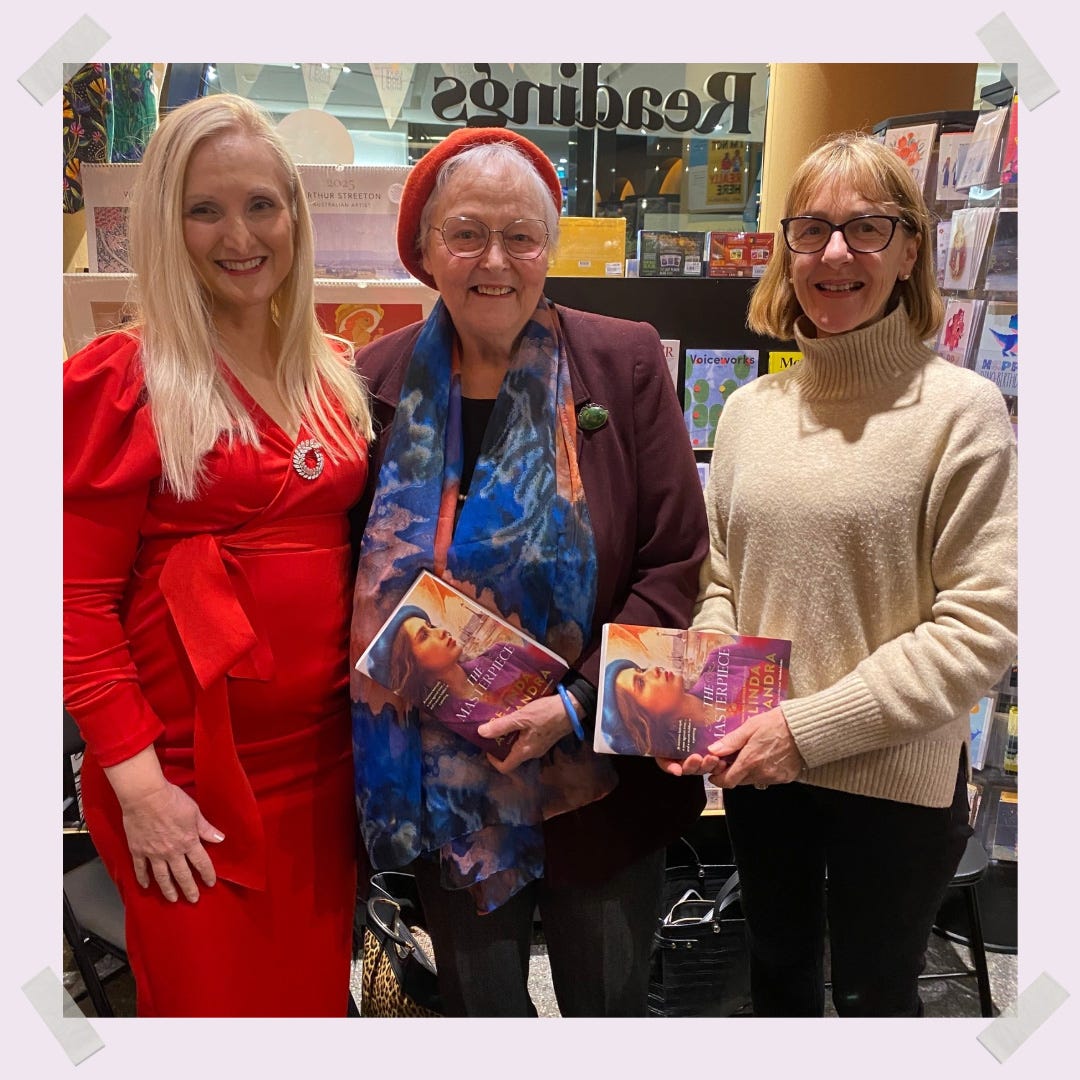 Belinda Alexandra smiles wearing a bright red dress with two gorgeous women (who hold copies of The Masterpiece) who came to see her at Readings books book event