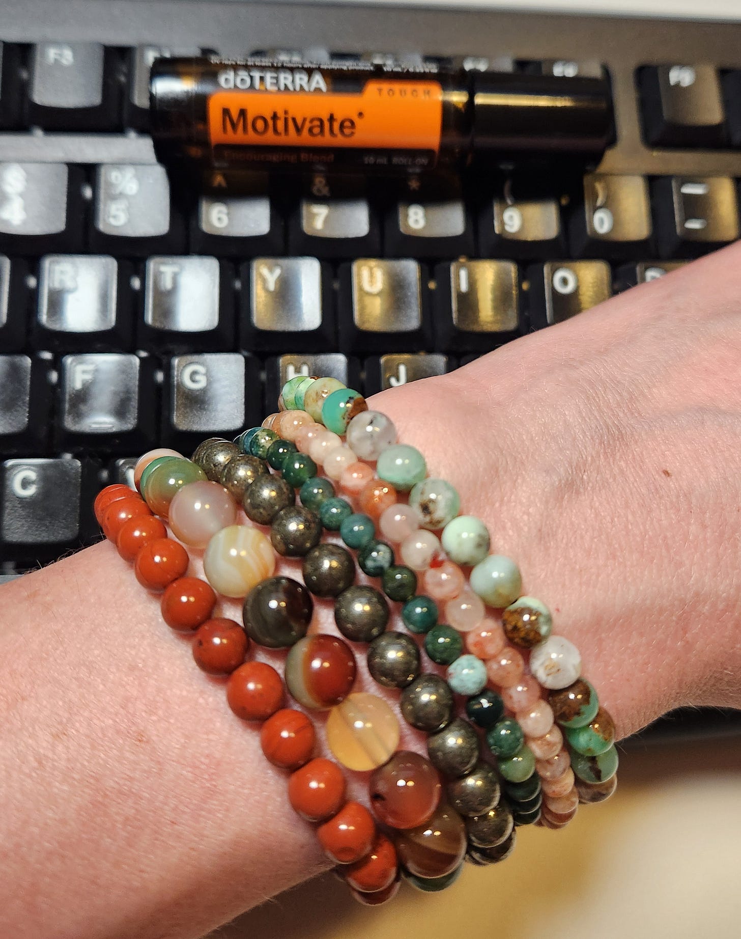 a stack of beaded bracelets on a wrist; a vial of doTERRA essential oil in ‘Motivate’ blend a stack of beaded bracelets on a wrist; a vial of doTERRA essential oil in ‘Motivate’ blend