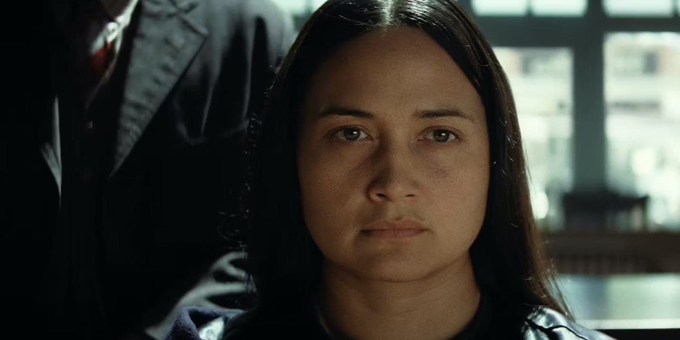 Movie still from Killers of the Flower Moon. A closeup of Mollie looking serious, a man standing behind her.