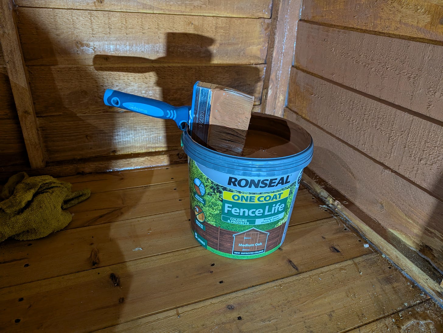 a pail of wood stain with a blue handled brush on top