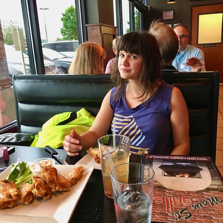 Jess sits at a table with a plate of chicken wings; in another picture the bike is parked in a lot while it rains