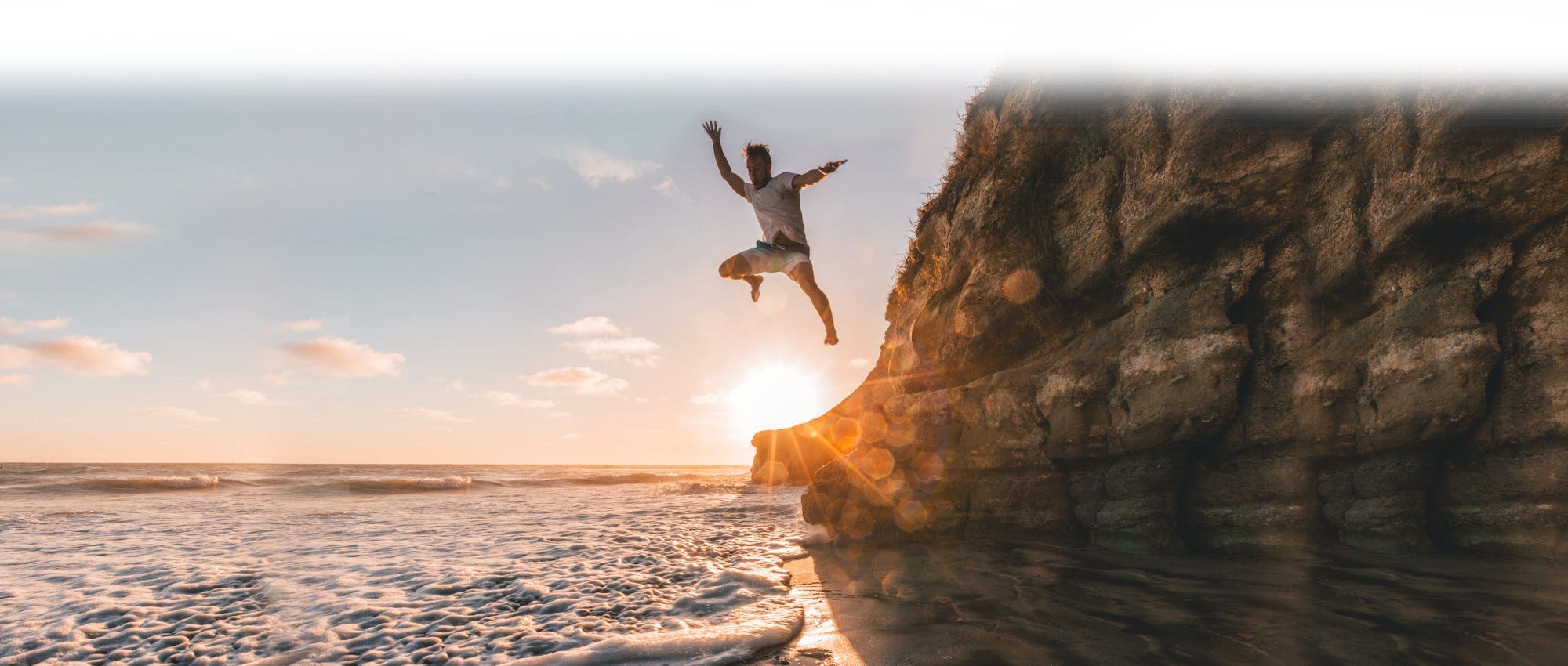 A guy jumping off a cliff into the water at sunset A guy jumping off a cliff into the water at sunset