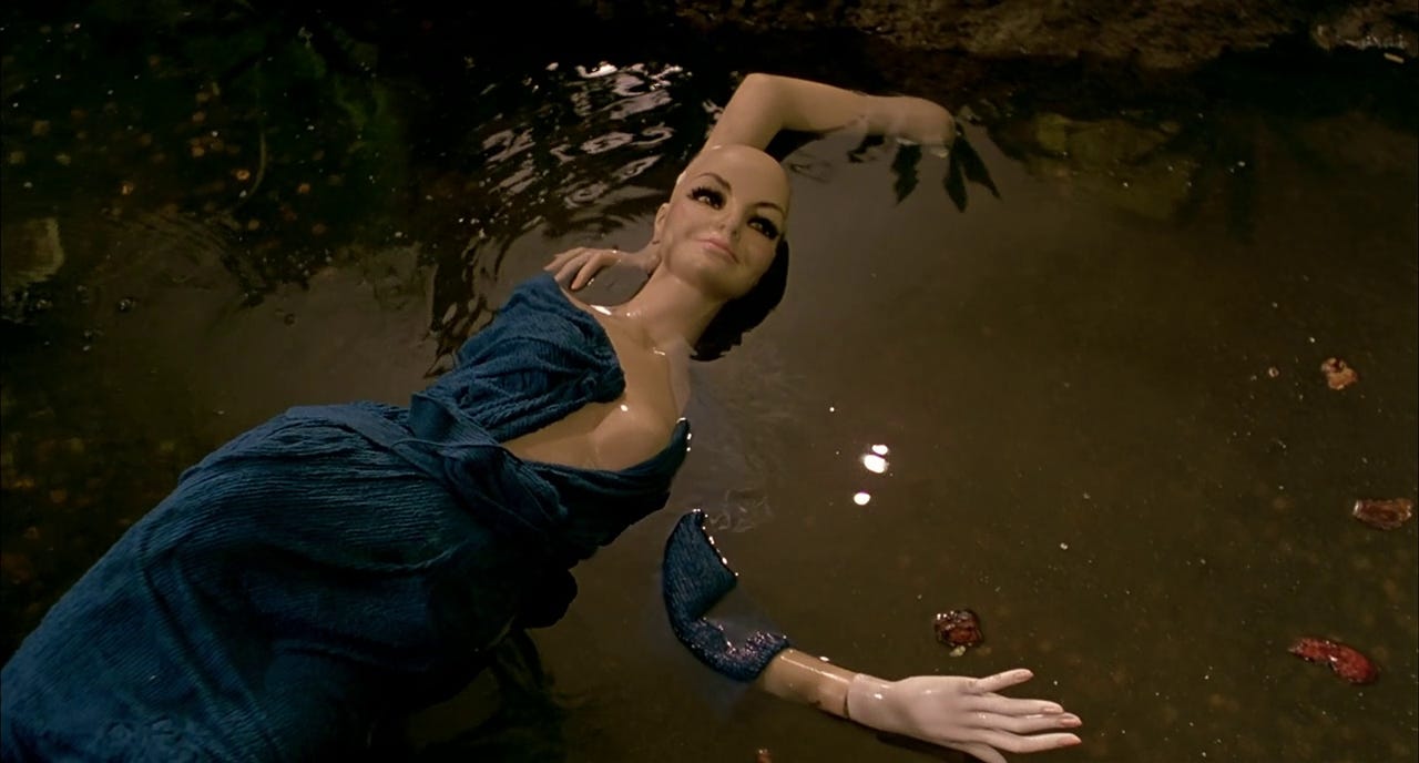 A partially-clothed mall mannequin lies, dismembered, in a pool of blood and other liquids.