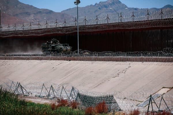 A military vehicle patrolling along layers of fencing and razor wire, with mountains in the background. A military vehicle patrolling along layers of fencing and razor wire, with mountains in the background.