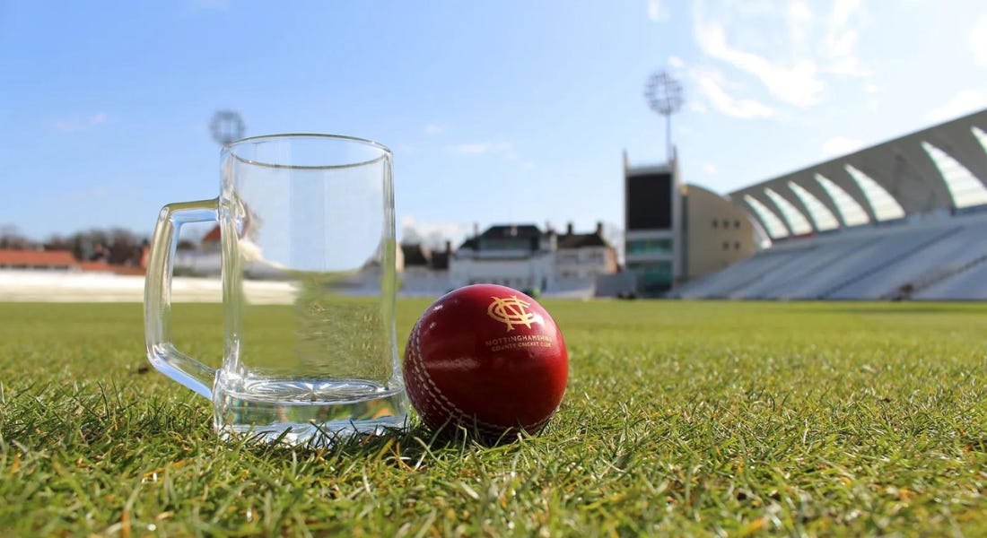 A glass tankard and a red cricket ball on a cricket pitch with seats around it A glass tankard and a red cricket ball on a cricket pitch with seats around it