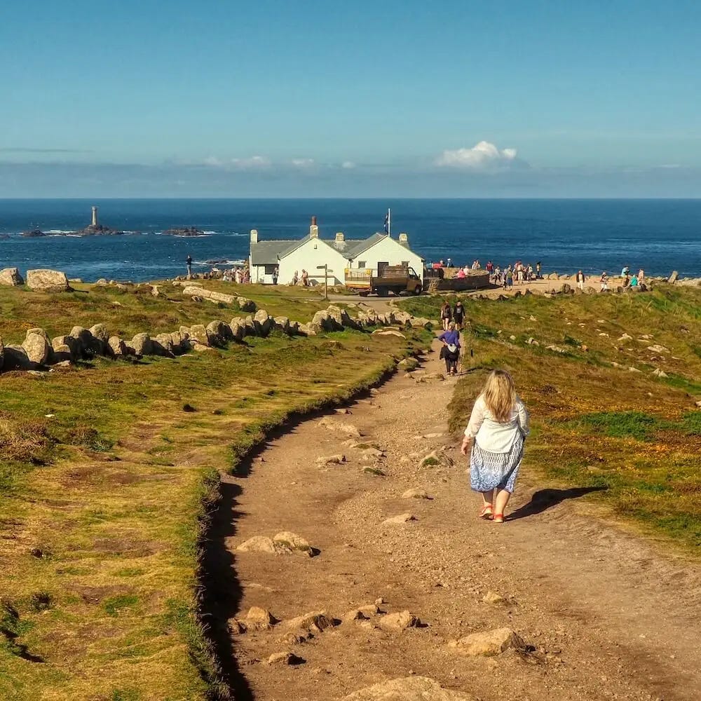 A footpath leads to a white building above cliffs and the sea