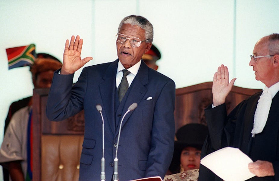 A man wearing a suit and tie raises his right hand to take an oath, wtacxhed by a male judge. A man wearing a suit and tie raises his right hand to take an oath, wtacxhed by a male judge.