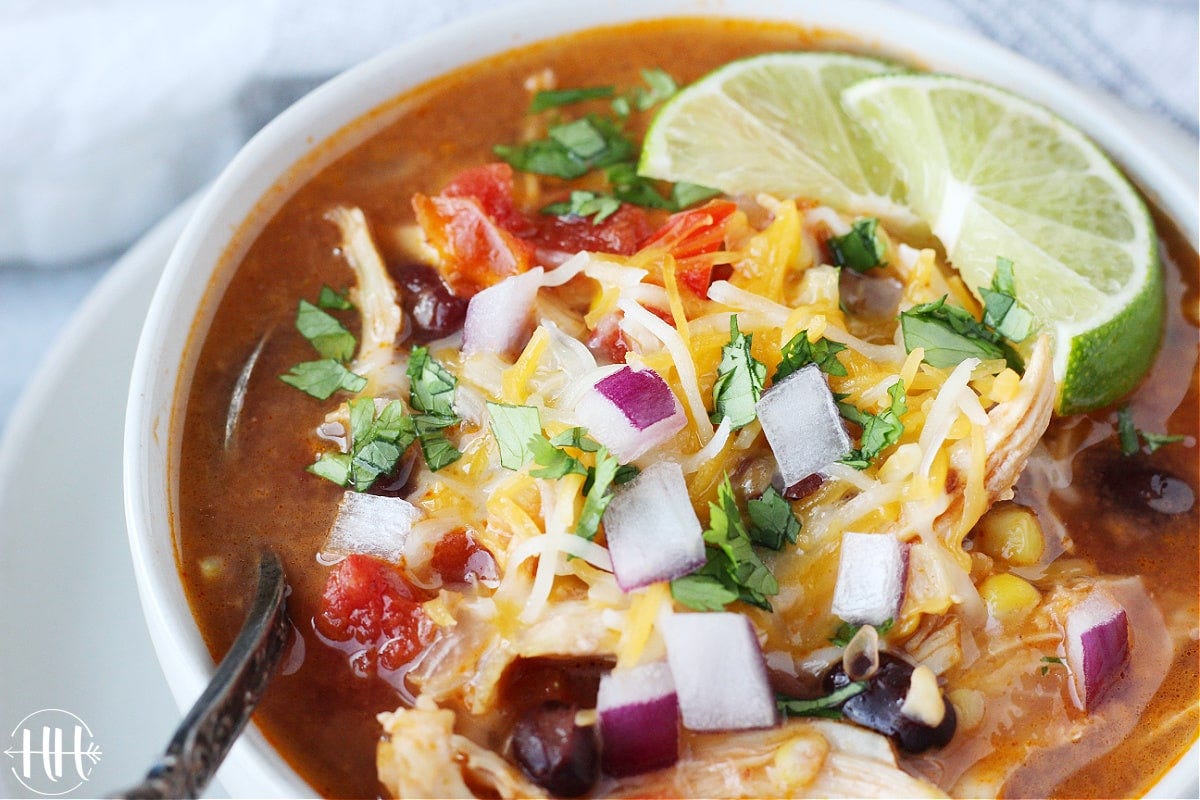 Diced red onion, shredded cheese and lime wedges on top of enchilada soup.