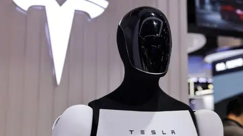Reuters Tesla's Optimus humanoid robot stands in front of a sign displaying the company's logo. Reuters Tesla's Optimus humanoid robot stands in front of a sign displaying the company's logo.