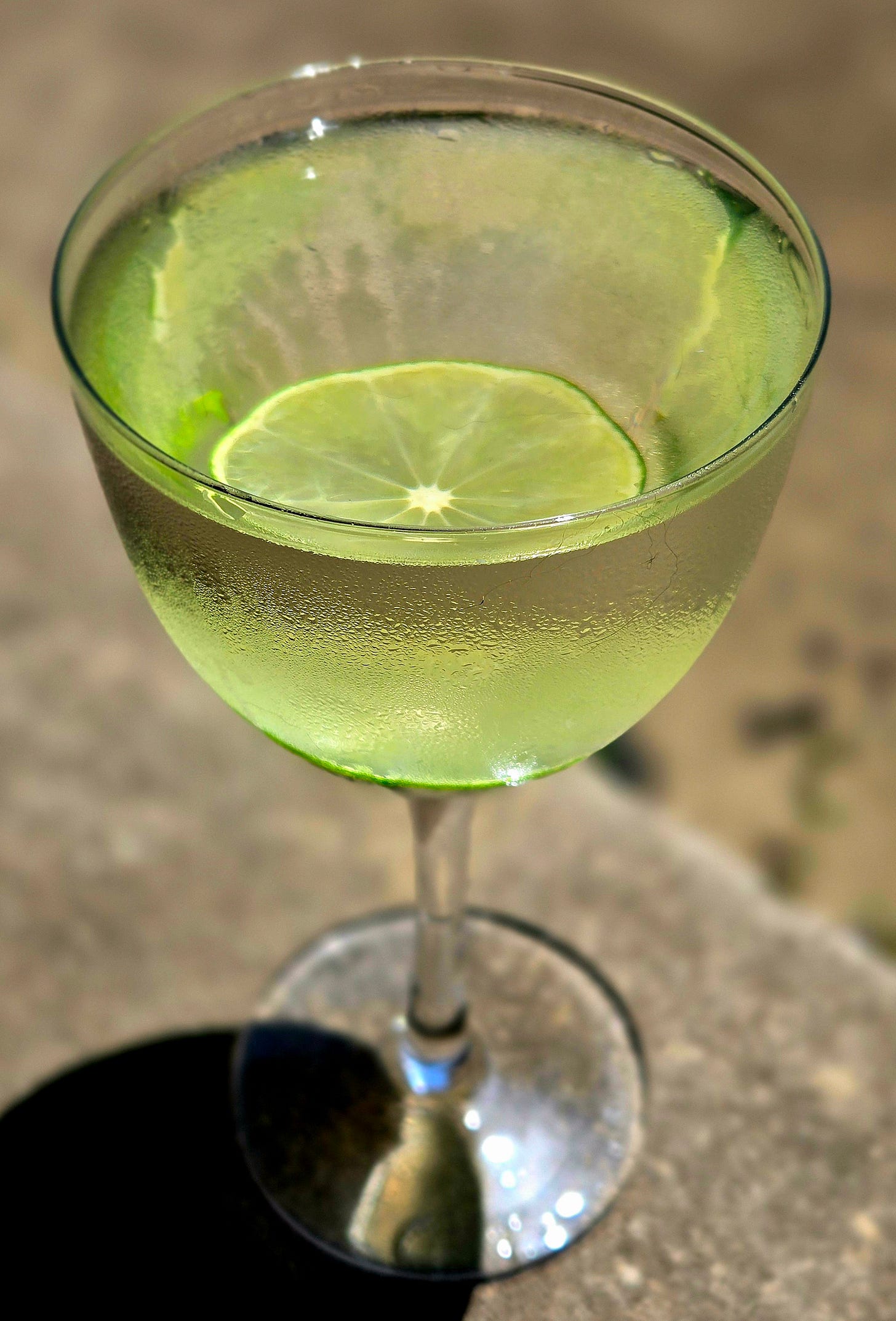 L’Étoile Libre cocktail in a Nick and Nora glass with think lime wheel garnish sitting atop a stone wall. L’Étoile Libre cocktail in a Nick and Nora glass with think lime wheel garnish sitting atop a stone wall.