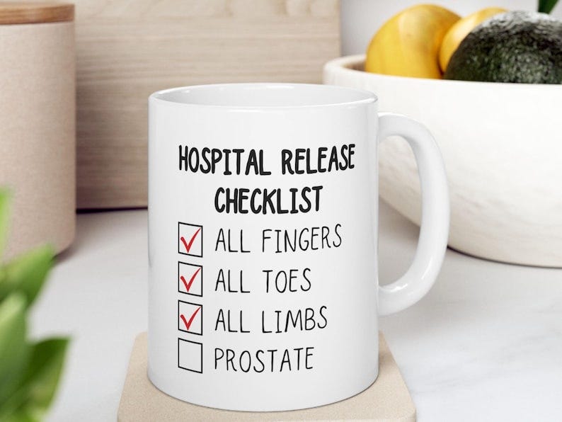 May include: A white coffee mug with black text that reads 'Hospital Release Checklist' with a checklist of items including 'All Fingers', 'All Toes', 'All Limbs', and 'Prostate'.