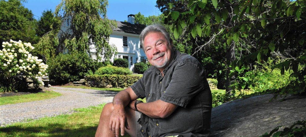 Image of a smiling man sitting outside a beautiful garden in front of a white house