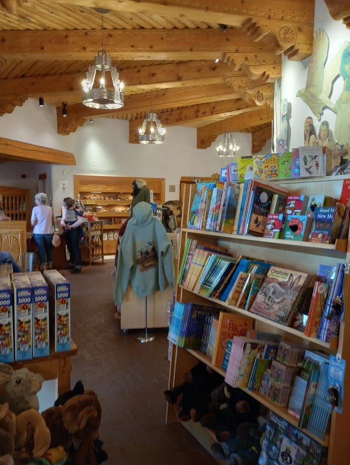 Gift shop with books and souvenirs, museum displays including basketry and diorama of the Pecos Pueblo, view from cloister of semi-desert with trees
