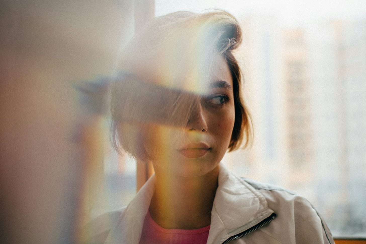 Thoughtful woman looking out window with soft light reflections, symbolizing career change, uncertainty and starting over. Photo by Egor Ivlev on Unsplash