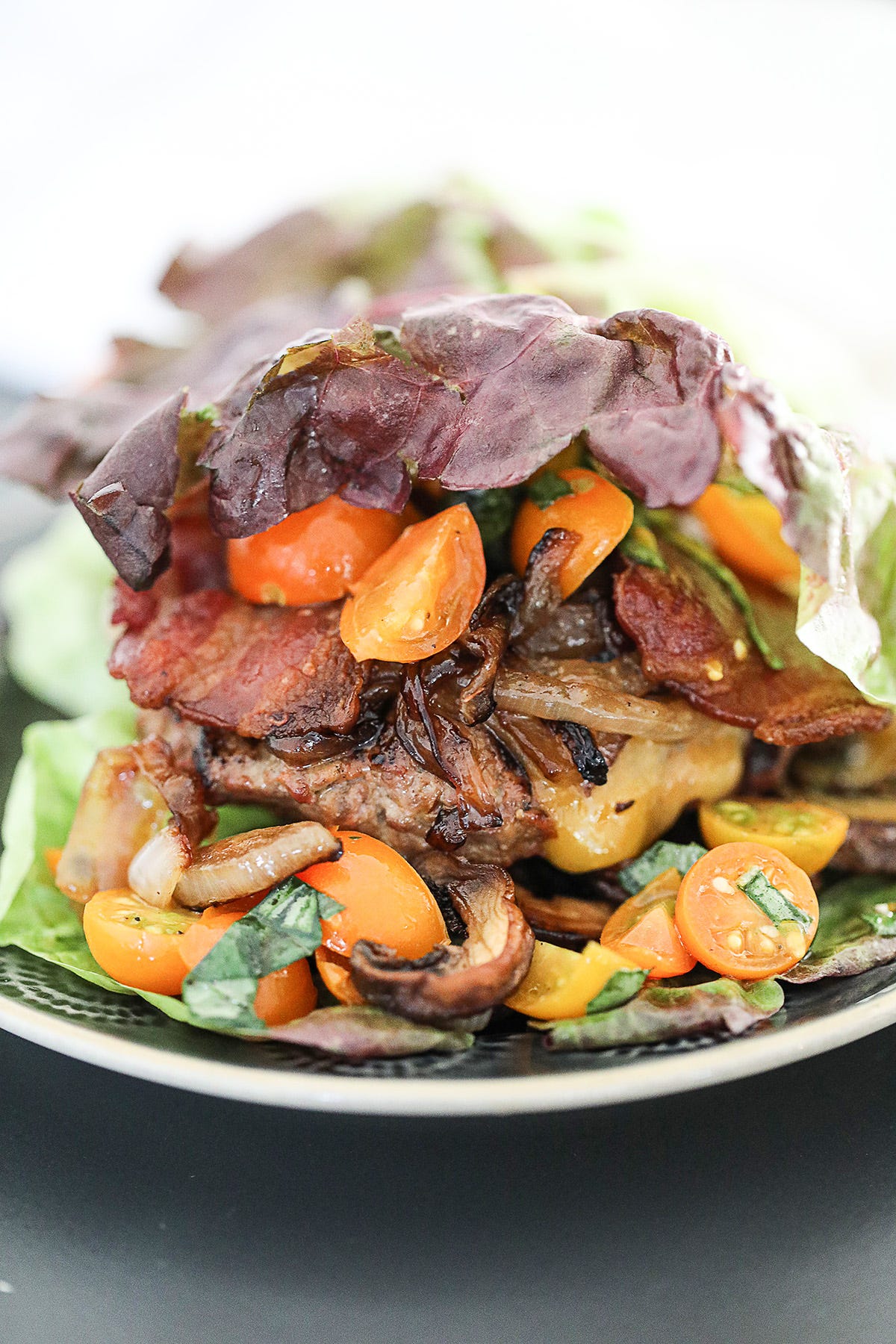 loaded burger wrapped in lettuce with crispy bacon, sautéed caramelized onions, mushrooms, cherry tomatoes, and melted cheese