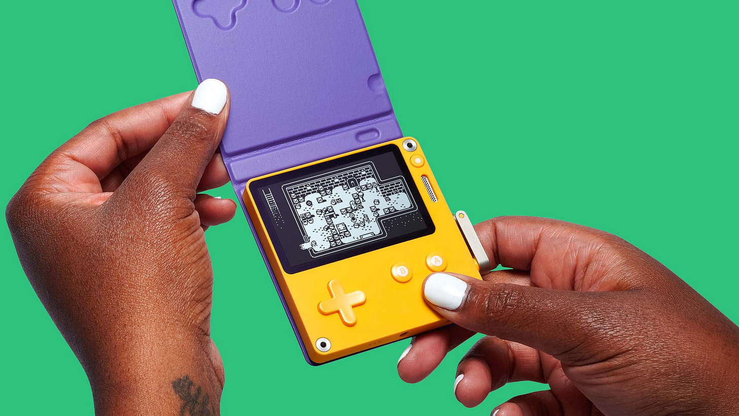 A pair of hands holding the Playdate, which looks small. There is a game playing on the black-and-white screen. The Playdate has a purple cover attached, meant to protect the screen when not in use.