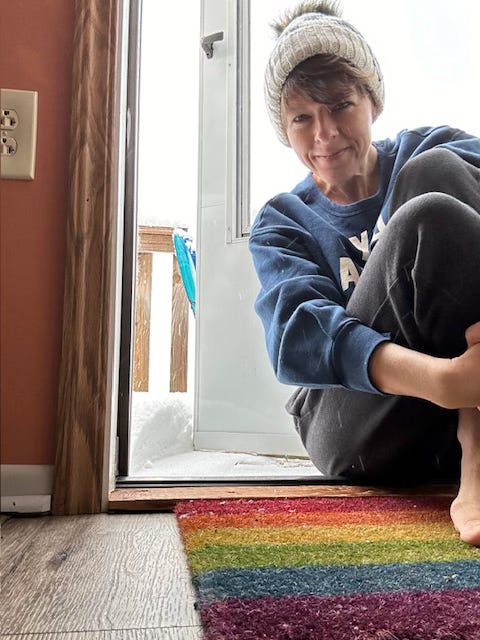Woman sitting on the floor in front of a white metal door open to the outside with three inches of snow on the ground. Woman sitting on the floor in front of a white metal door open to the outside with three inches of snow on the ground.