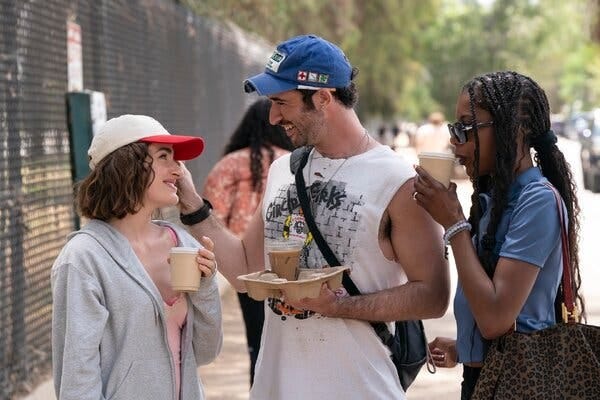 Two women and a man smile outside, holding coffees