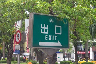 A sign that says exit in both Chinese and English in a tropical city scene A sign that says exit in both Chinese and English in a tropical city scene
