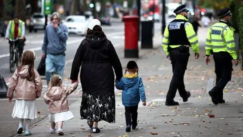 Getty Images A family including two young girls in white dresses and pink coats along with a little boy in a blue coat. They walk down the street with their backs to the camera and in the background two Metropolitan Police officers in uniform can be seen walking in the same direction.