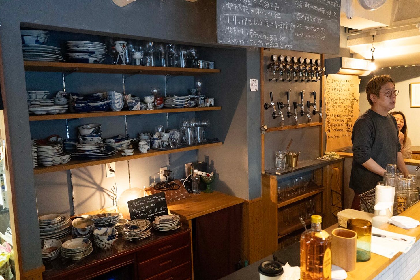 Futa-san holds court behind the bar, his dad's crockery across three shelves, a chalk board menu of his daily creations above his head and a small wall of craft beer taps behind him