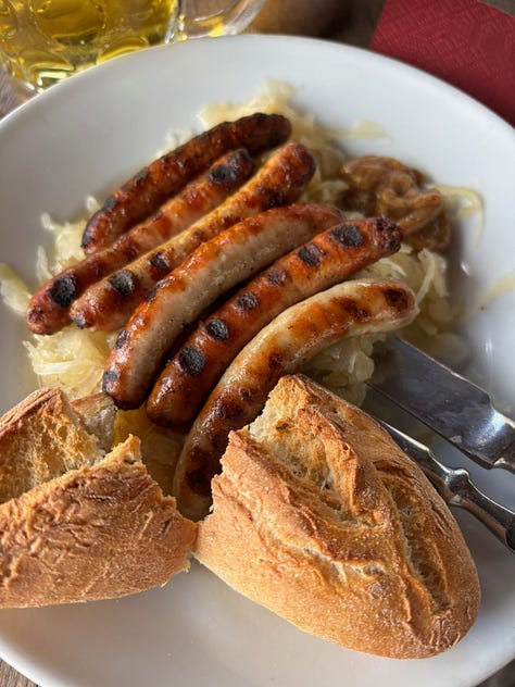 a gothic cathedral, man holding a mug of beer, a plate of sausages and bread, building by a river, a wall of cuckoo clocks, closeup of a christmas musical piece in the cuckoo shop