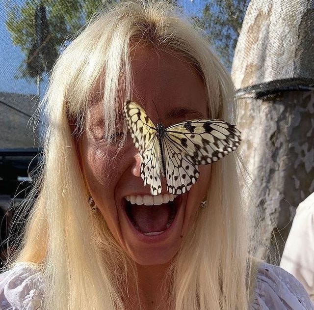 This may contain: a woman laughing with a butterfly on her face in front of her eyes and mouth wide open