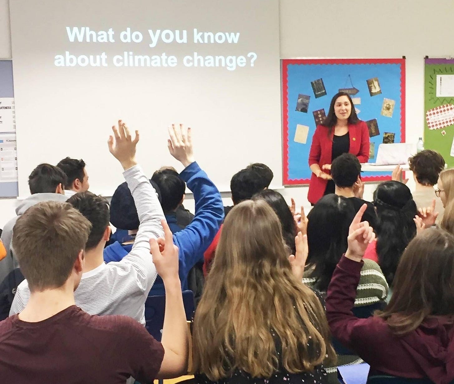 Bradlie stands at the front of a classroom of young teens by a Powerpoint slide that says 'What do YOU know about climate change?' Bradlie stands at the front of a classroom of young teens by a Powerpoint slide that says 'What do YOU know about climate change?'