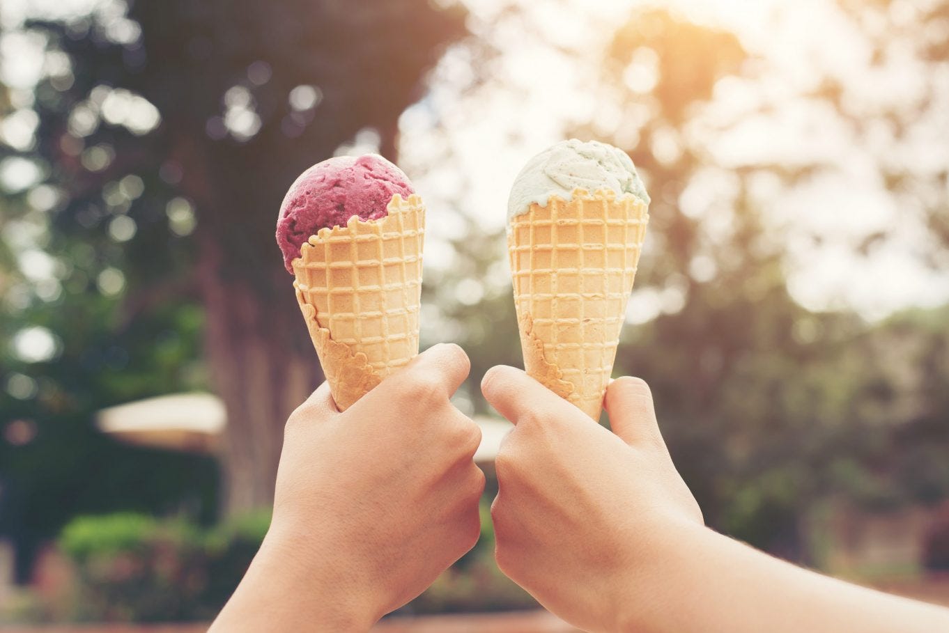 Two ice cream cones, one with purple ice cream and one with green ice cream, held by two hands. Image Source: Glazed Coffee & Creamery