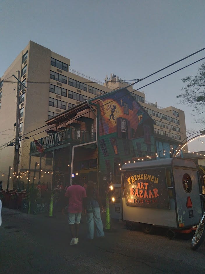 Street scene of the Spotted Cat Music Club and Frenchmen Art Bazaar at dusk.