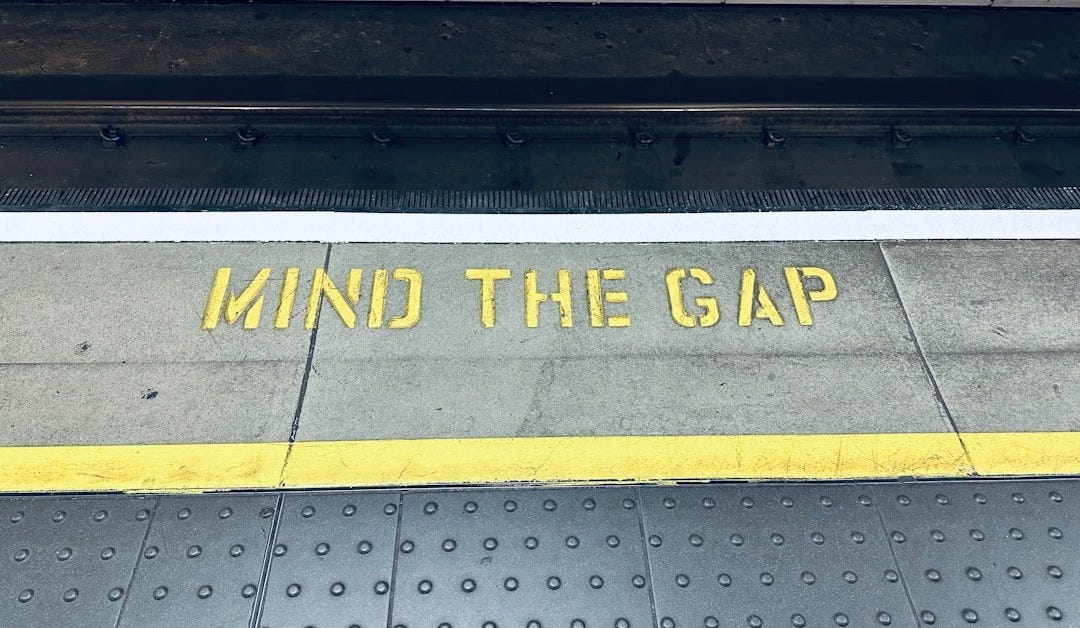 a sign that says mind the gap on the sidewalk