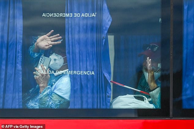 Passengers from the MV Hondius, including one with his mask lowered, wave aboard a military bus after being transferred by boat to the industrial port of Granadilla de Abona on the island of Tenerife