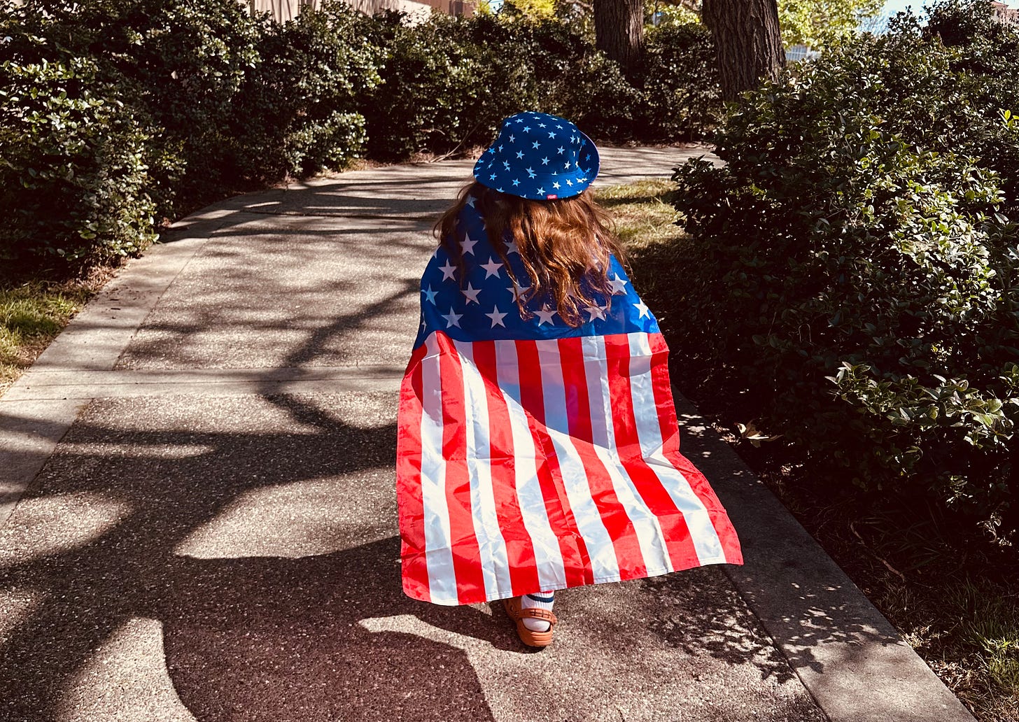 child walking in tribute to Memorial Day wearing patriotic American Flag cape with rsvlts bucket hat