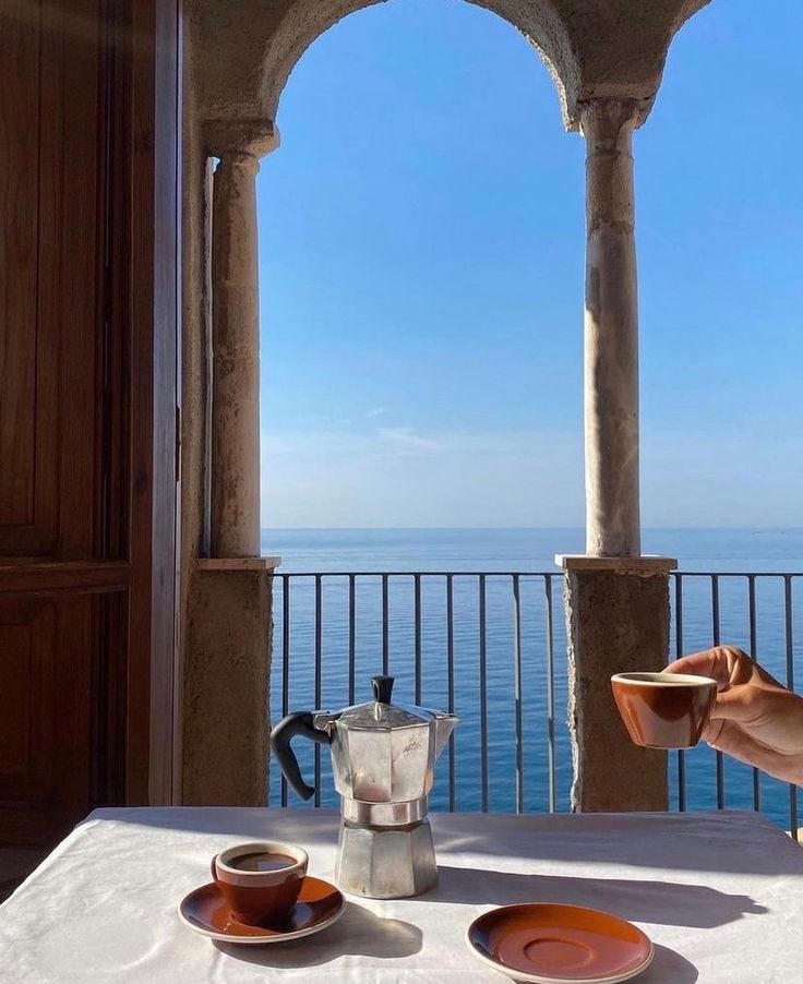 This may contain: a person sitting at a table with two cups and saucers in front of the ocean