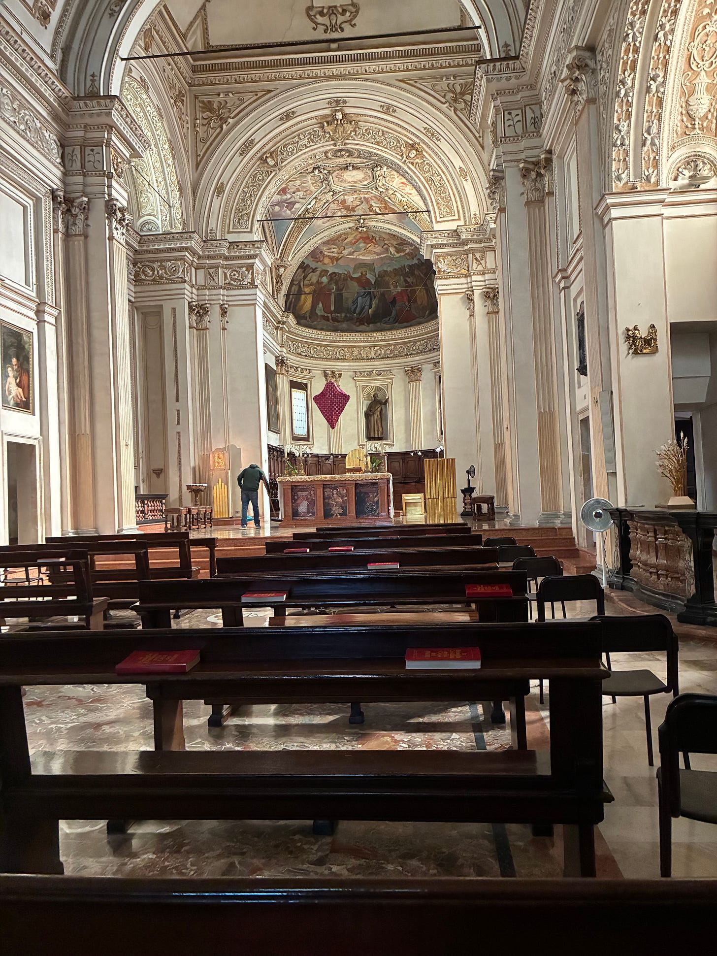 Interno della chiesa di San Barnaba a Milano, navata vuota con panche in legno e, in fondo all'altare, un drappo rosso a rombo che copre il crocifisso.
