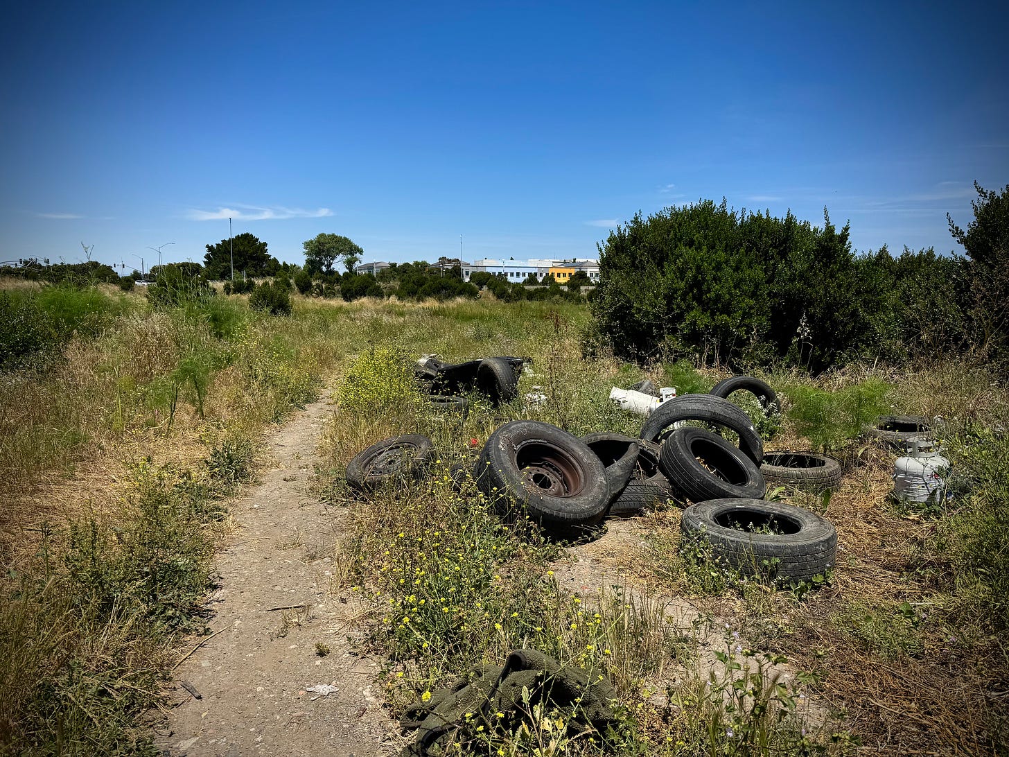 Old tires dumped by a Jeep road in empty lot; Meta corporate headquarters visible in background
