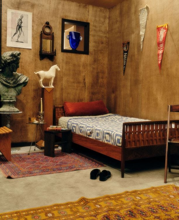 This may contain: a bed room with a neatly made bed next to a table and two statues on the wall This may contain: a bed room with a neatly made bed next to a table and two statues on the wall