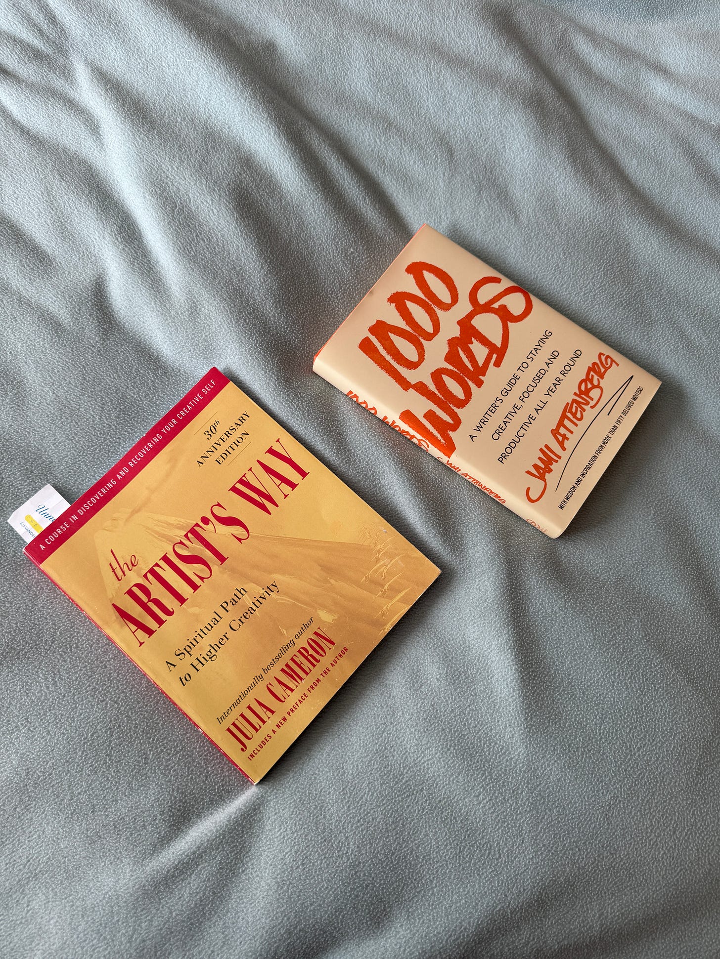 The Artist's Way and 1000 Words books laid out on a bed