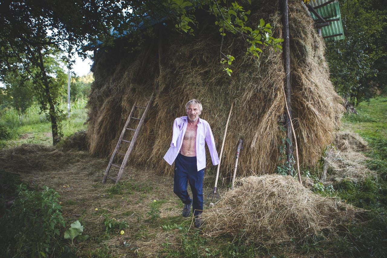 Szuhányi outside his home; behind him is a large pile of hay that he adds to each day.