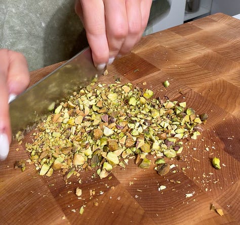 Whipped ricotta in a food processor with a spatula, Finely chopped pistachios and thinly sliced fresh mint being chopped on a wooden cutting board for skewer topping
